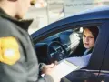 Policjant wręcza kobiecie w samochodzie mandaty w Austrii. Kobieta wygląda na zmartwioną.