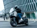 Mężczyzna w kasku jedzie skuterem Yamaha X-MAX 125 po mieście. Czy to lepszy wybór niż Honda Forza 125?