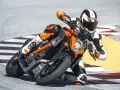 Motocyklista w kombinezonie ściga się na torze na pomarańczowym KTM 1290 Super Duke, pochylony w zakręcie.