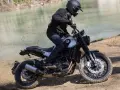 Motocyklista w kasku i czarnej kurtce jedzie motocyklem Benelli Leoncino 500 Trail po piaszczystym brzegu rzeki, wzbijając tumany kurzu.