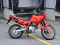 Czerwony motocykl Honda Dominator z lat 90. stoi na asfalcie. Ma złote felgi i czarne siedzenie.