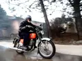 Mężczyzna w kasku i goglach jedzie na pomarańczowym motocyklu WSK. Widać dym z rury wydechowej.