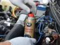 Ręka w rękawiczce trzyma puszkę płukanki do silnika motocyklowego K2 Motor Flush, gotowa do użycia w silniku.
