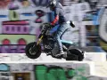 Młody człowiek na elektrycznym motocyklu BMW CE02 skacze nad przeszkodą na tle kolorowego graffiti.