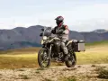 Motocyklista w kasku i stroju podróżuje na motocyklu BMW 800 GS po piaszczystej drodze, w tle górzysty krajobraz.