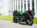 Zielony Kawasaki Ninja H2 z czarnymi kuframi, gotowy do podróży obok nowoczesnego budynku.