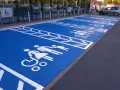 Niebieski parking z białymi symbolami osób na wózkach inwalidzkich i rodzin. Znak P19 informuje o przeznaczeniu miejsc.