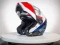 Kask motocyklowy z podniesioną szczęką, w kolorach białym, czerwonym i niebieskim, na białym tle.