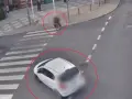 Biały samochód wymusza pierwszeństwo na pasach, omal nie potrącając pieszego z walizką. Inny samochód zatrzymał się przed przejściem.
