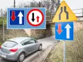 Znaki drogowe informują o pierwszeństwie na zwężonym odcinku jezdni. Samochód zbliża się do miejsca, gdzie ruch jest utrudniony.