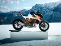Pomarańczowo-biały KTM Super Duke na śnieżnym tle z górami w tle.