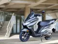 Szary skuter Suzuki Burgman 125 na tle nowoczesnego budynku z betonowymi schodami.