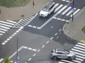 Skrzyżowanie dróg z przejściami dla pieszych i samochodami. Jeden biały SUV i srebrny crossover czekają na zielone światło.