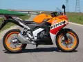 Pomarańczowy motocykl Honda CBR 125 Repsol na drodze. Warto sprawdzić honda cbr 125 dane techniczne przed zakupem.