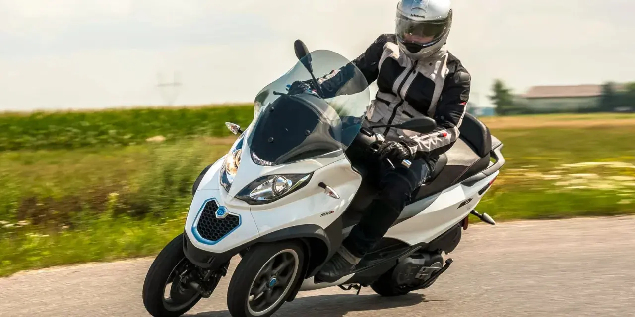 Biały Piaggio MP3 500 z kierowcą w kasku pędzi po drodze. Zastanawiasz się nad jego spalaniem?