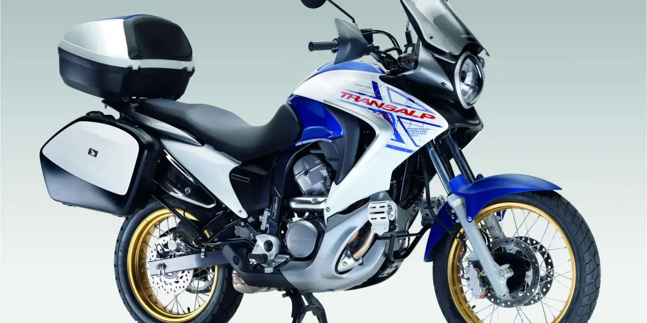 Honda Transalp 700 dane techniczne: turystyczny motocykl z kuframi, biało-niebieski, złote felgi, gotowy na przygodę.