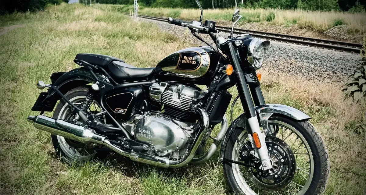 Czarny Royal Enfield Classic 650 lśni chromem na tle torów kolejowych i zieleni. Gotowy na przygodę.