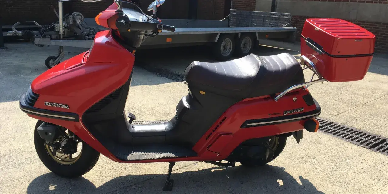 Czerwony skuter Honda Spacy 250 z kufrem, gotowy do podróży.