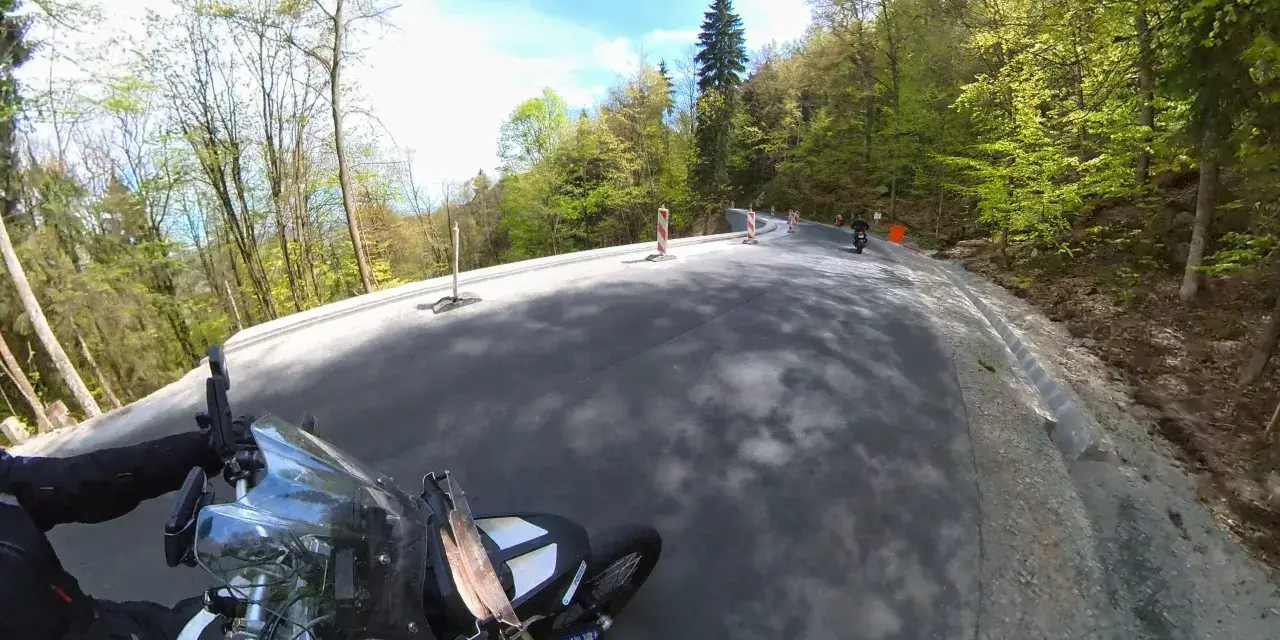 Motocyklista pokonuje zakręty na malowniczej drodze stu zakrętów, otoczonej zielonymi lasami.
