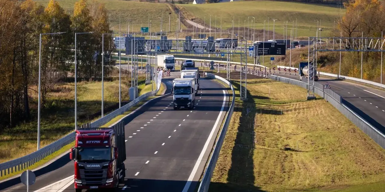 Ciężarówki na Via Baltica w jesiennym krajobrazie. Droga szybkiego ruchu z wieloma pojazdami, w tym czerwonym Scanią.