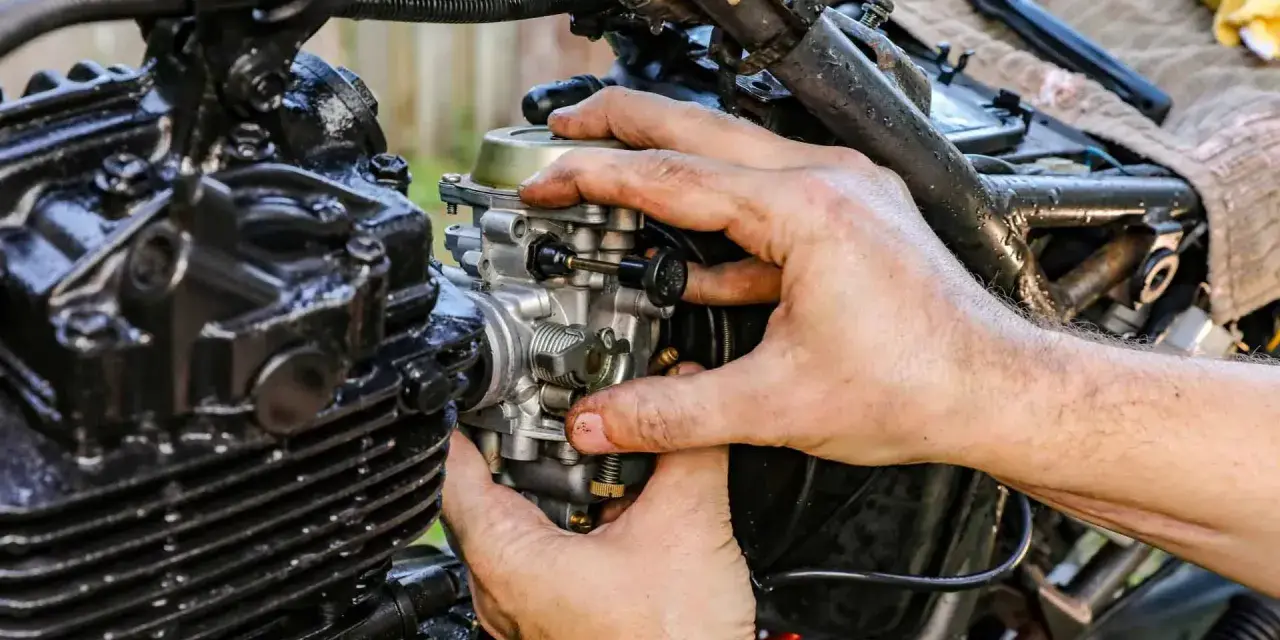 Dłonie mechanika regulują gaźnik motocykla, kluczowy element odpowiedzialny za symbol ssania paliwa i powietrza.