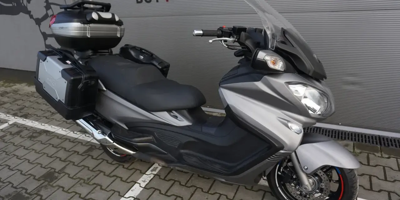 Srebrny Suzuki Burgman 650 Executive z kuframi, gotowy na dalekie podróże.