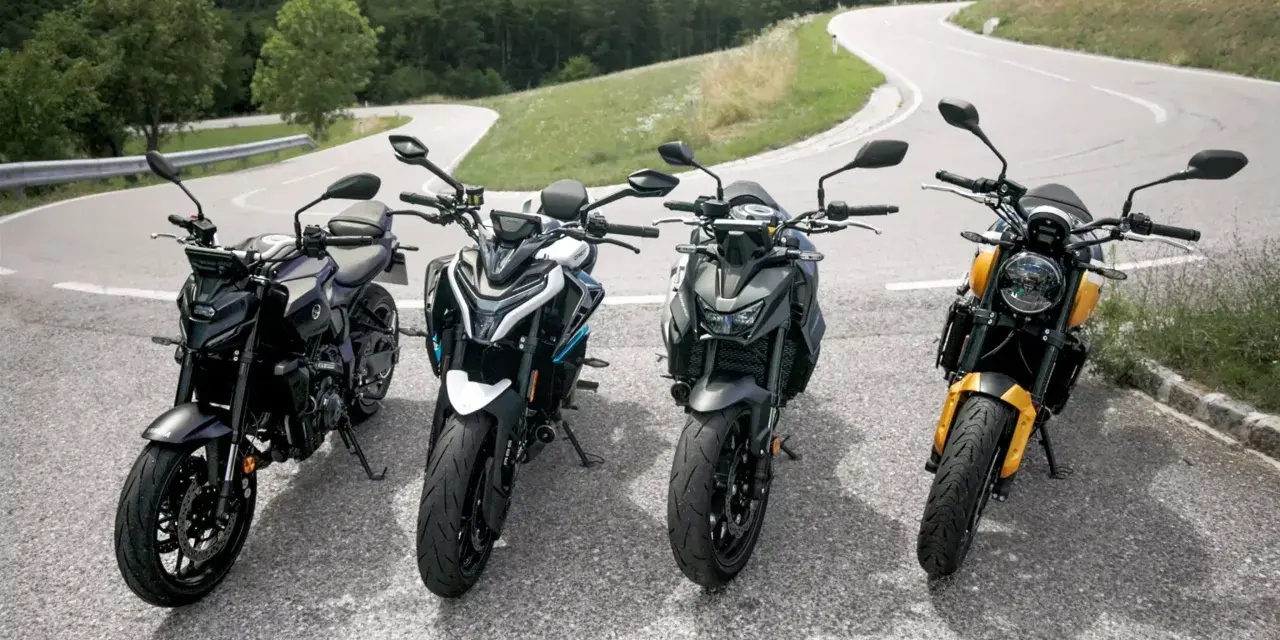 Cztery motocykle typu naked stojące na zakręcie górskiej drogi.