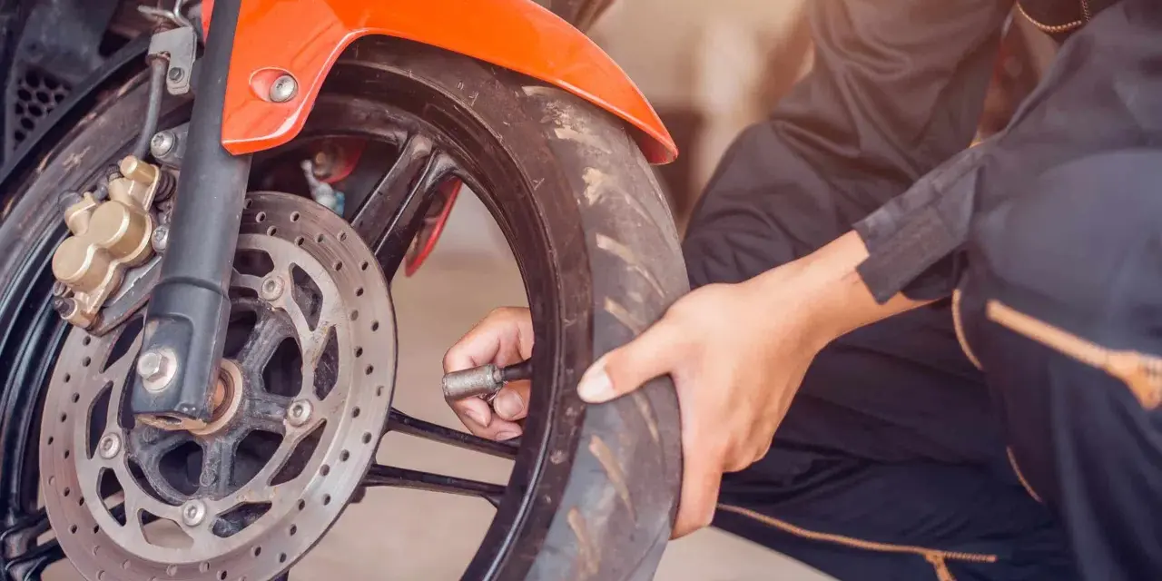 Sprawdzanie, jakie ciśnienie w oponach motocykla jest kluczowe dla bezpieczeństwa. Dłoń z manometrem przy wentylu przedniego koła.