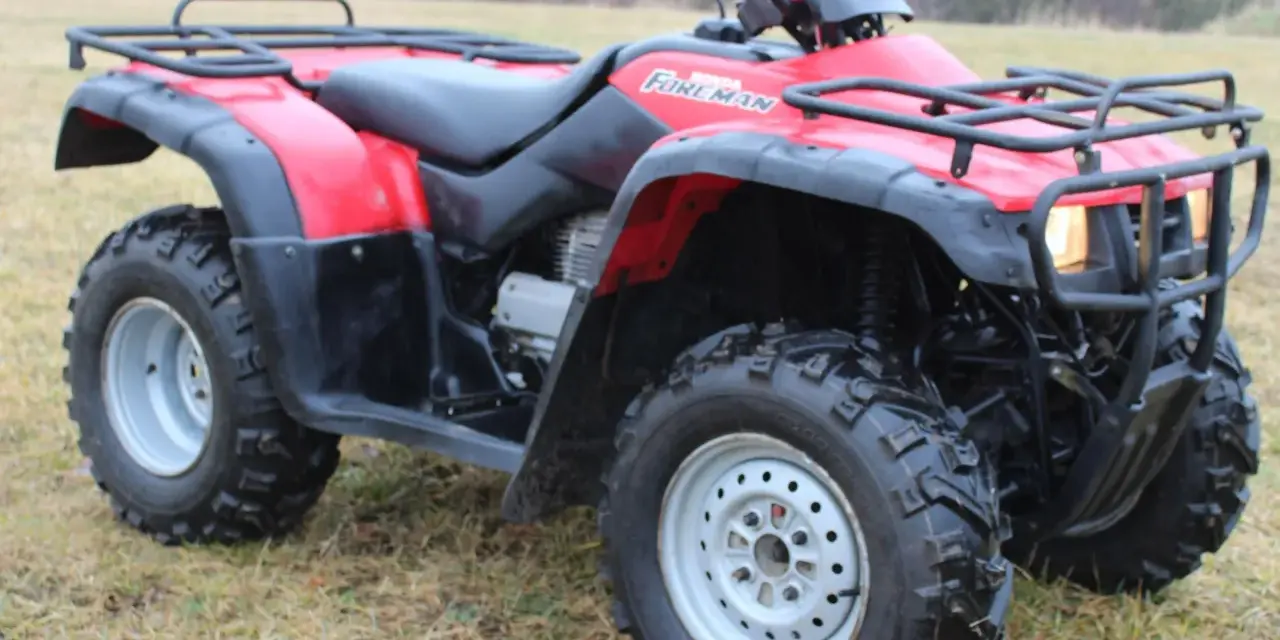 Czerwony quad Honda TRX 350 Foreman gotowy do jazdy po nierównym terenie.