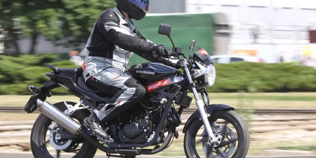 Motocyklista w kasku i kombinezonie jedzie na czarnym motocyklu Hyosung GT 125.