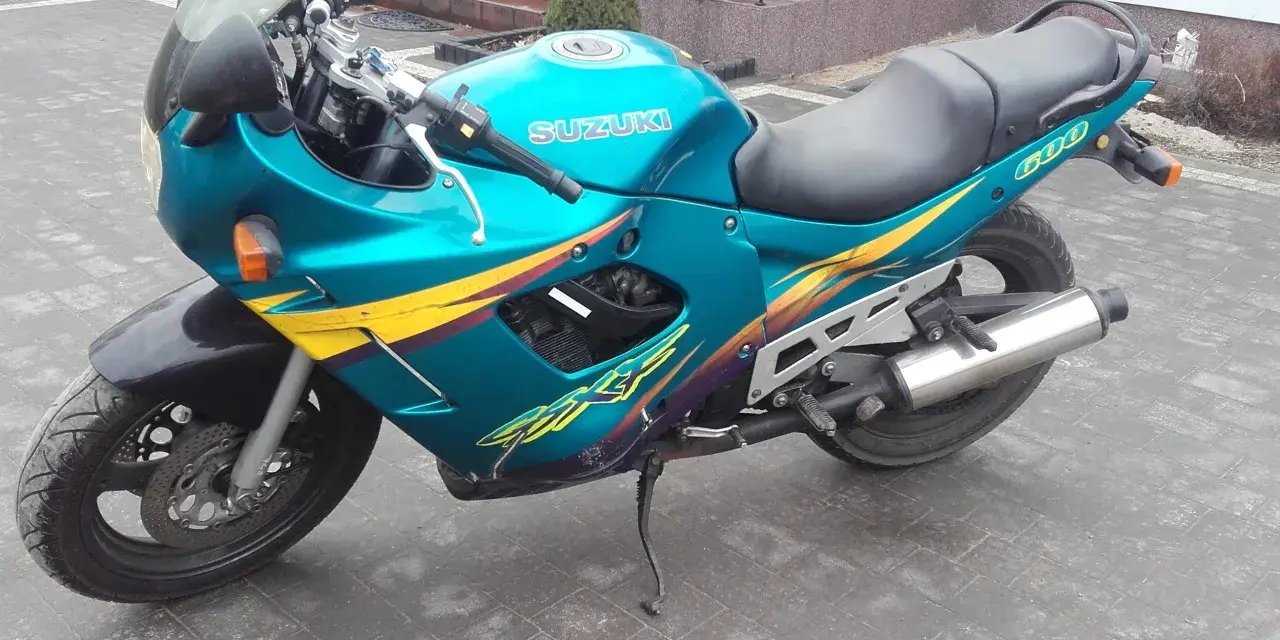 Turkusowy Suzuki GSXF 600 z żółto-fioletowymi grafikami, zaparkowany na kostce brukowej przed domem.