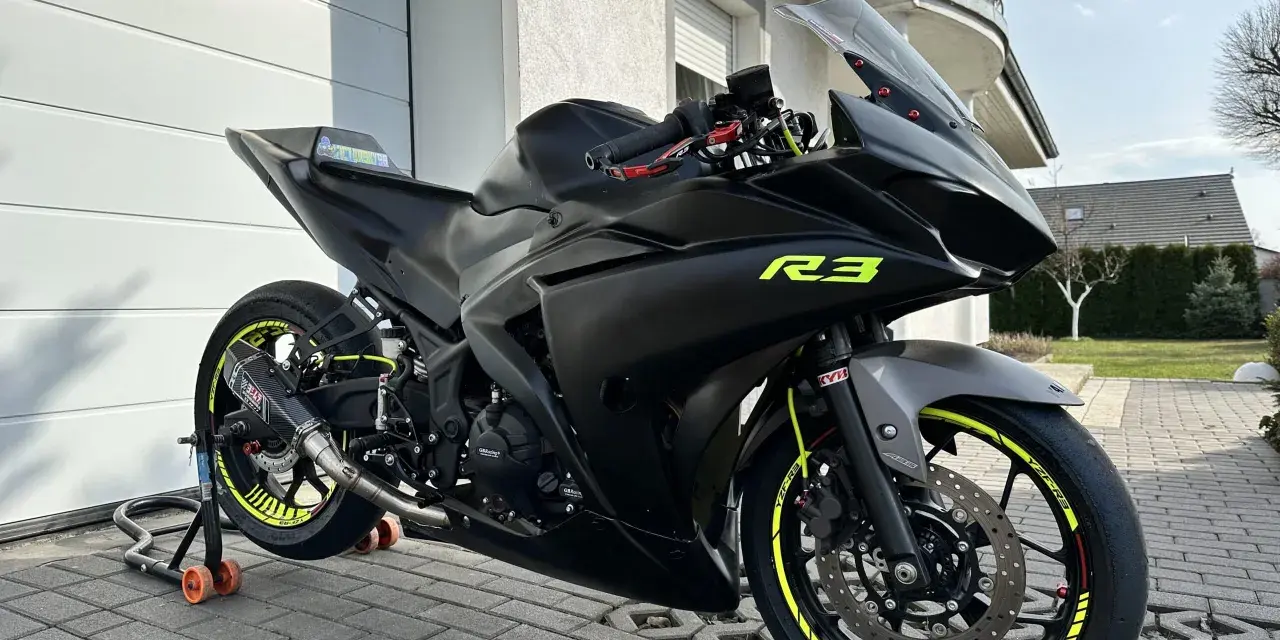 Czarny motocykl Yamaha R3 z żółtymi akcentami na felgach i owiewkach. Widać sportowy wydech Yoshimura. Idealny do poznania yamaha r3 dane techniczne.