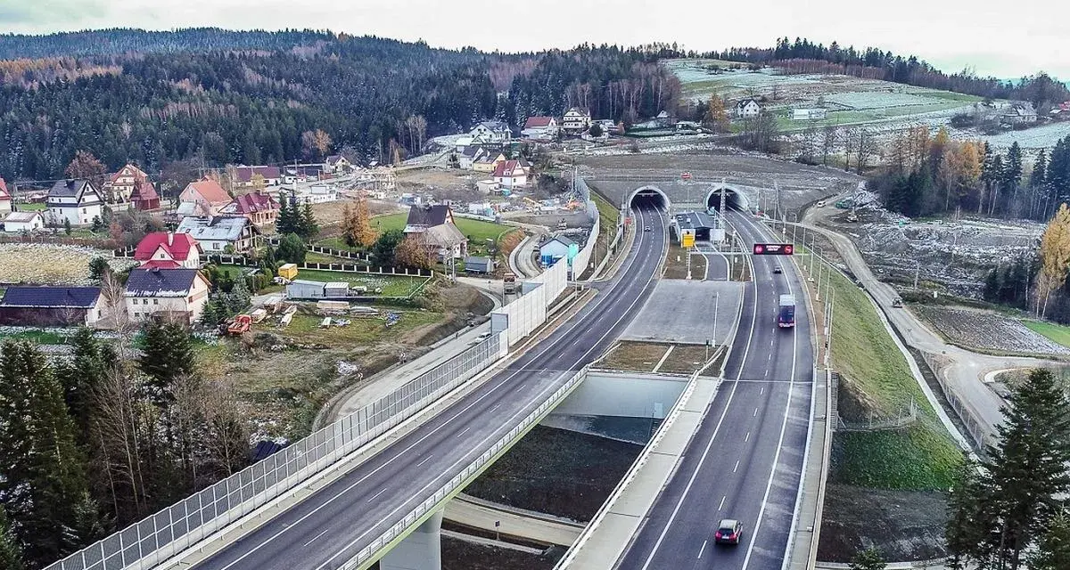 Nowa zakopianka trasa z tunelami i wiaduktami, otoczona lasami i zabudowaniami.