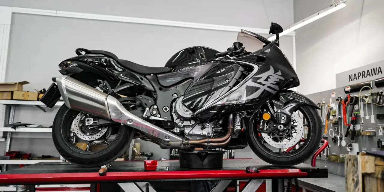Czarny, lśniący motocykl typu naked bike na podnośniku w warsztacie. W tle tablica z narzędziami i napis "NAPRAWA".