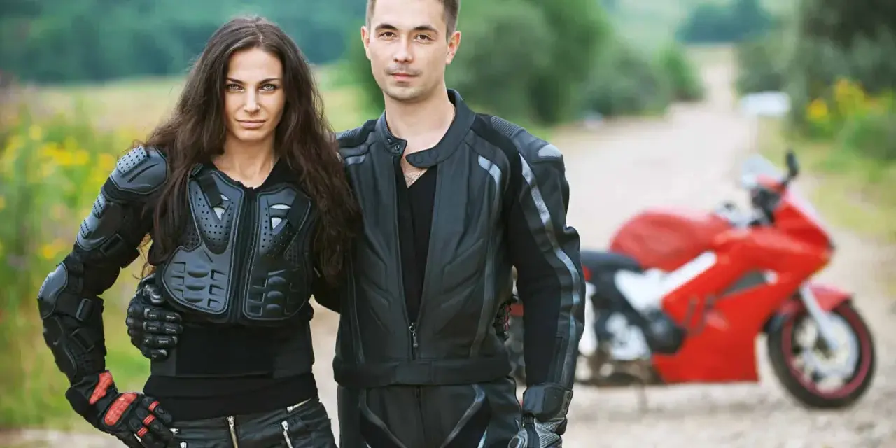 Para gotowa na jazdę na motorze. Ona w zbroi, on w skórzanej kurtce. Czerwony motocykl czeka.