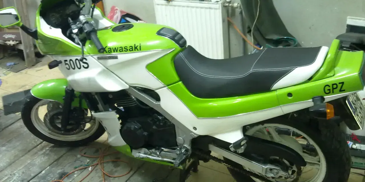 Zielono-biały motocykl Kawasaki GPZ 500 z napisem "GPZ" na tyle. Stoi na drewnianej podłodze w garażu.