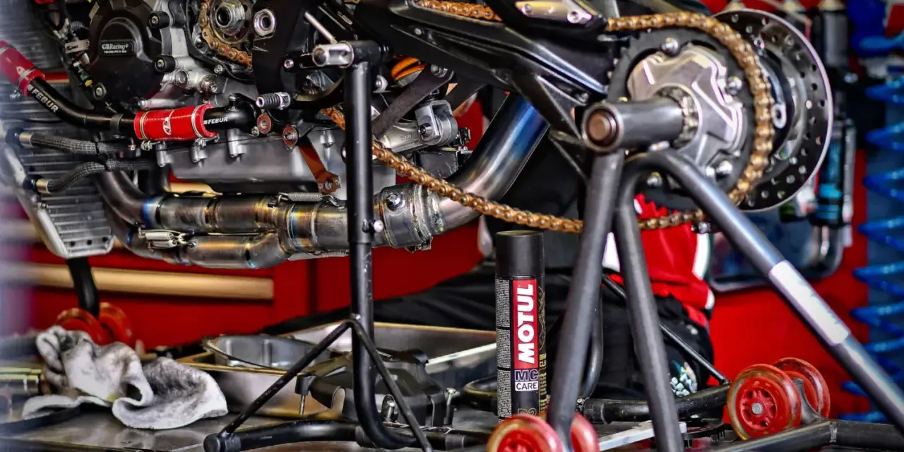 Motocykl na stojaku, widoczny napęd i łańcuch. Puszka smaru Motul sugeruje, co ile smarować łańcuch w motocyklu.