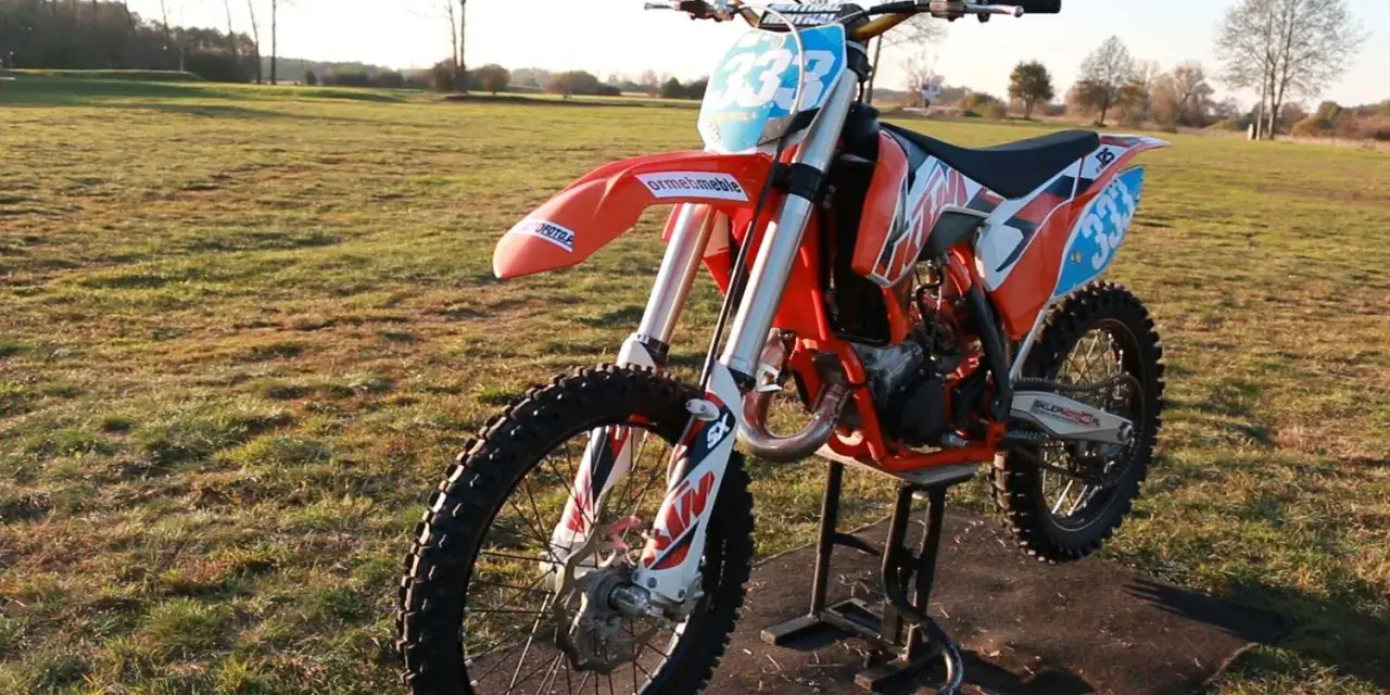 Pomarańczowy motocykl KTM SX 125 na stojaku, gotowy do jazdy. Zastanawiasz się, ile koni ma KTM SX 125? Ten model to potęga na torze!