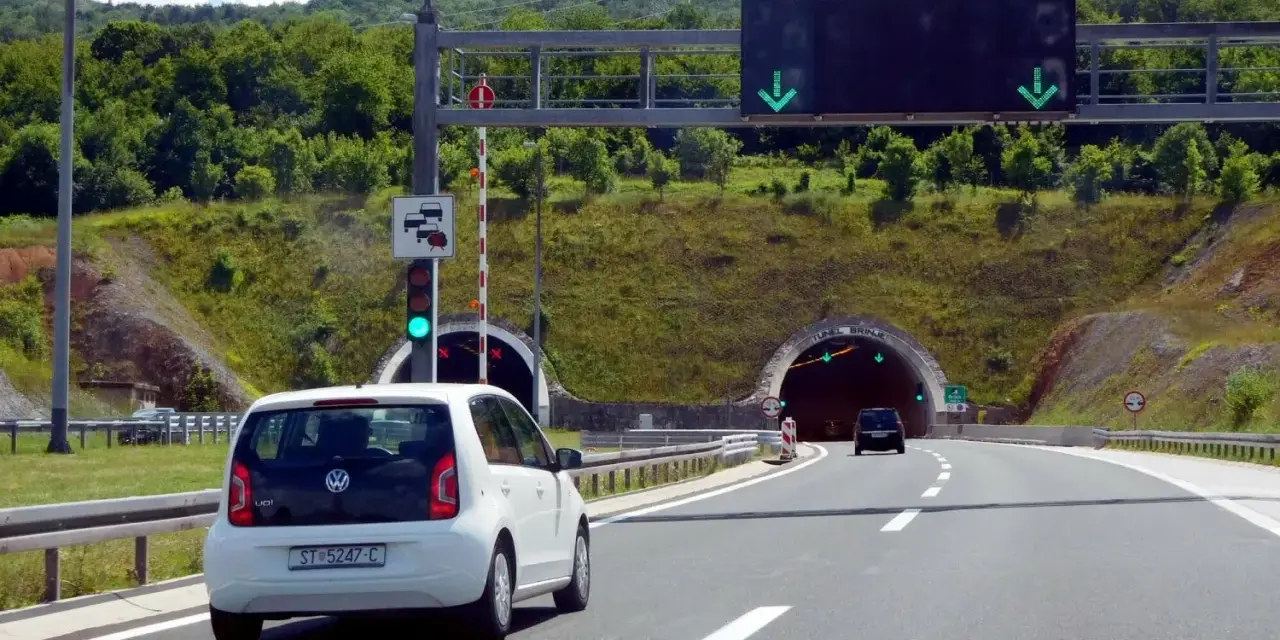 W Chorwacji są płatne autostrady. Biały samochód zbliża się do tunelu, sygnalizacja świetlna zielona.