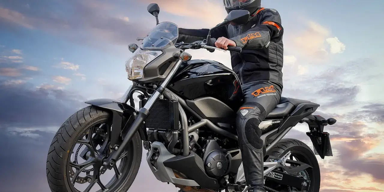 Motocyklista w kasku i kombinezonie siedzi na czarnym motocyklu. Idealny motor na kat B, gotowy na przygodę.