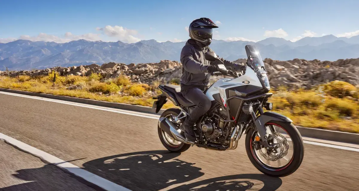 Motocyklista na białym Honda CB500X przemierza malowniczą, górską drogę.