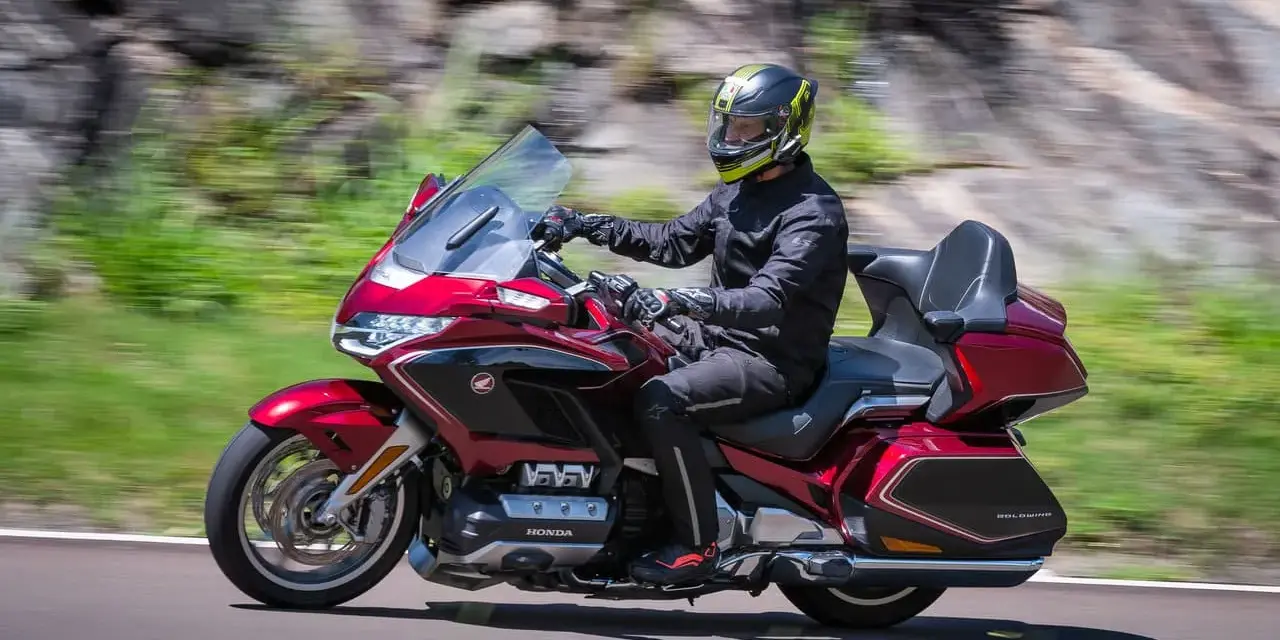 Mężczyzna w kasku jedzie lśniącym, czerwonym motocyklem Honda Gold Wing, uznawanym za najlepszy motocykl turystyczny.