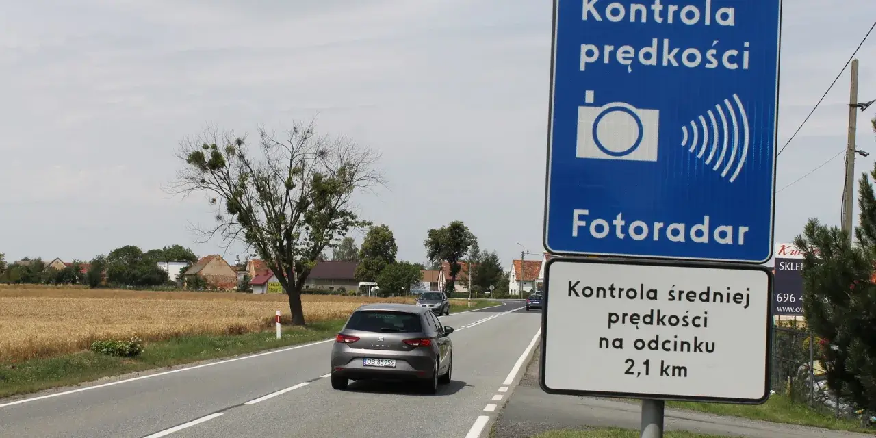 Znak "Kontrola prędkości Fotoradar" informuje, że czy fotoradar musi być oznakowany. Obok droga i pola.