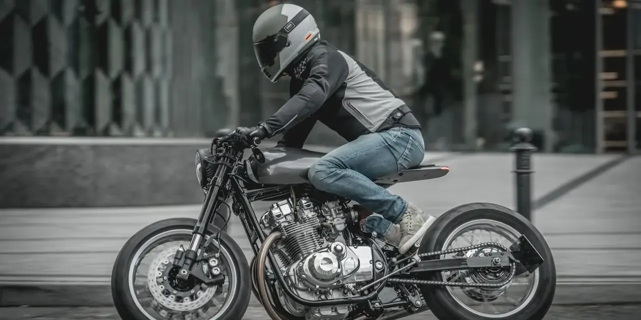 Motocyklista w kasku i jeansach pędzi na stylowym Suzuki GS 650 po miejskiej ulicy.