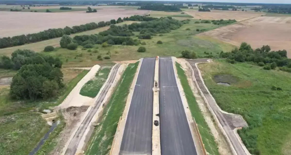 Budowa drogi ekspresowej S2 Siedlce-Biała Podlaska. Nowa nawierzchnia asfaltowa w otoczeniu zieleni i pól.