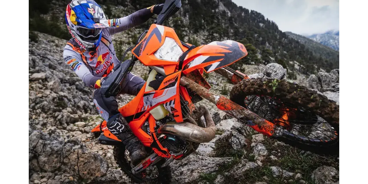 Motocyklista w kasku Red Bull na pomarańczowym KTM EXC 300 2T pokonuje kamienisty teren. Dane techniczne tego potwora terenowego są imponujące.