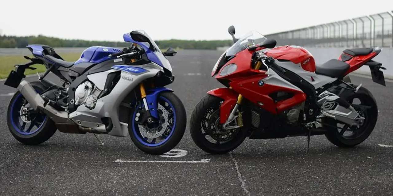 Dwa sportowe motocykle: niebiesko-srebrny Yamaha R1 i czerwono-biały BMW S1000RR 2020, stojące na torze wyścigowym.