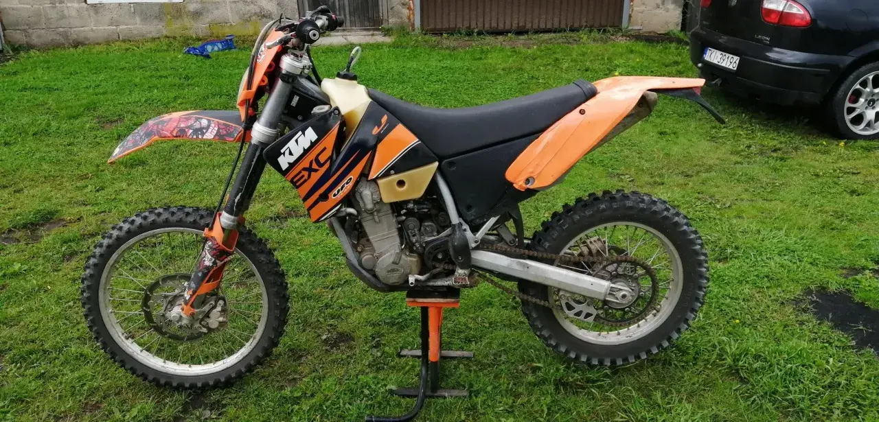 Pomarańczowy motocykl KTM 400 EXC na stojaku, gotowy do jazdy po bezdrożach.