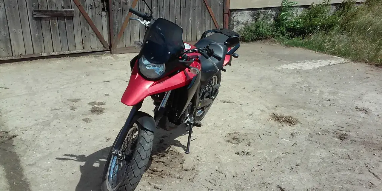 Czerwony motocykl Derbi Terra 125 stoi przed drewnianą stodołą.