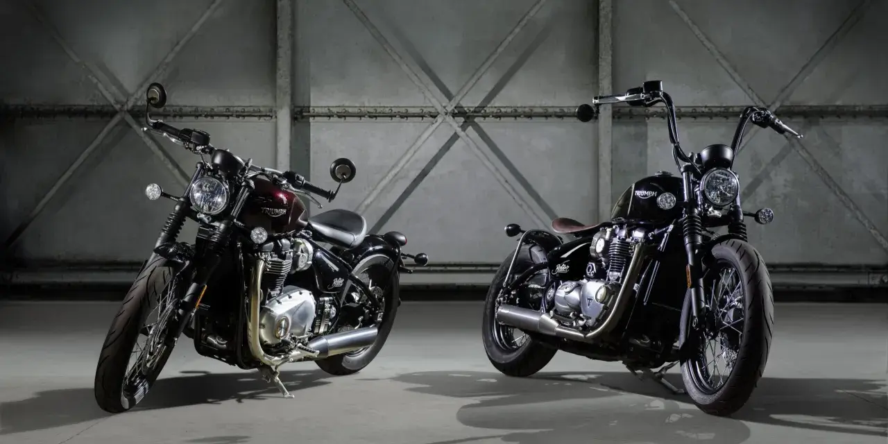 Dwa motocykle Triumph Bonneville Bobber w ciemnych kolorach, stojące obok siebie w industrialnym wnętrzu.